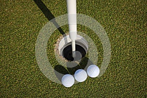 Three golf balls near hole on green field. photo