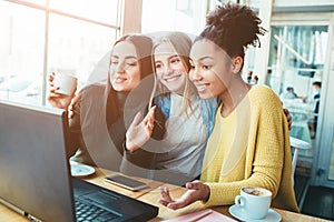 Three gourgeous best friends are in cafe. They are sitting vlose to a laptop which is on the table and loking to the