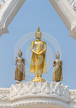 Three graceful and peaceful golden Buddha statues standing under beautiful white arch with blue sky background