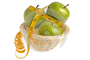 Three green apples wrapped with measuring tape in the wicker basket isolated