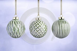 Three Green Ceramic Christmas baubles with gold ribbons on a light background.