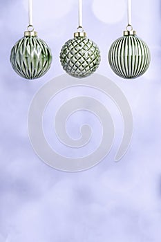 Three Green Ceramic Christmas baubles with gold ribbons on a light background.