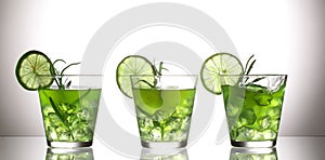 Three green cocktails with lemon and rosemary standing on glass in studio, gray background