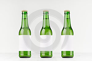 Three green longneck beer bottles 330ml with blank white label on white wooden board, mock up.