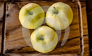 Three green organic healthy apples on wooden board.