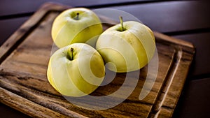 Three green organic healthy apples on wooden board.