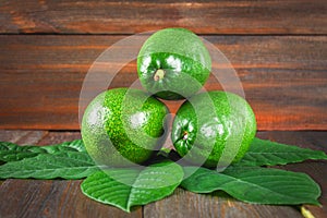 Three green raw ripe avocados with leaves lie on a wooden brown table.