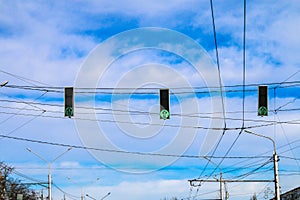 Three green traffic lights hang over the road against the blue sky. Allow signal.