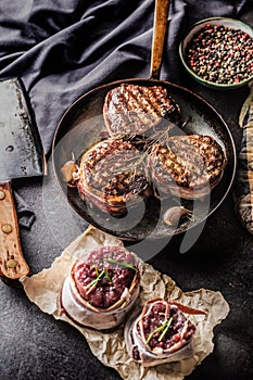 Three grilled beef tenderloin steaks coated bacon on a frying pa