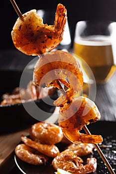 Three grilled shrimp on a stick with light beer glass