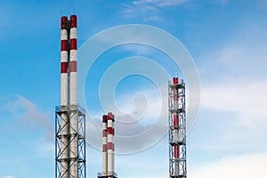 Three groups of red and white industrial pipes against a cloudy sky