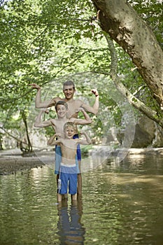 Three growing friends stand in the water and show their muscles during a summer camp in the forest