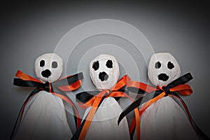 Three halloween ghosts DIY made from white tissue paper, black and orange ribbon on gray background