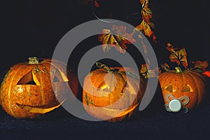 Three Halloween pumpkins with faces and candles inside on a dark background