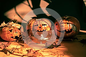 Three halloween pumpkins painted as Jack`s lantern, one in protective face mask, fall leaves, magic shadows. New normal