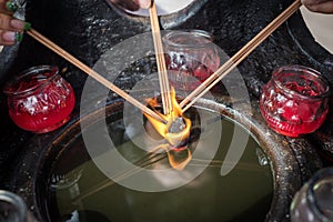 Three hand holding incense sticks over a burning candle