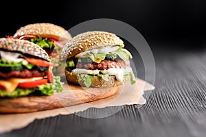Three handmade burgers with beef, salad, cheese tomatoes, sesame seeds, bacon on black wooden table