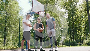 Three handsome sportsmen staying on the basketball court outdoors - man in black uniform holding the ball