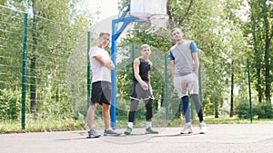 Three handsome sportsmen staying on the basketball court outdoors - one sportsman doing keepy-uppies