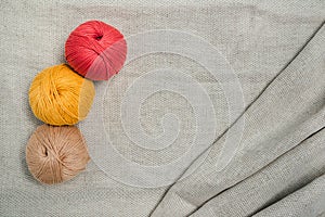 Three hanks of yarn, red, yellow and beige, on grey linnen fabric. Knitting, embriodering, crocheting and punch work