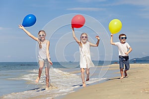 Three happy children with balloons playing on the beach at the d