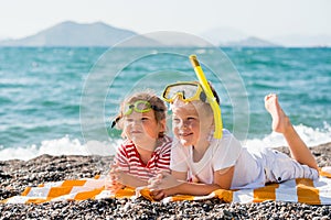 Three happy children on beach with colorful face masks and snorkels, sea in background. Summer vacation