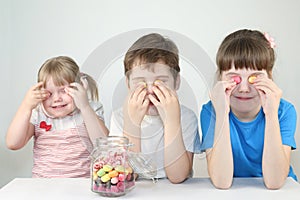 Three happy children close eyes by candies near jar