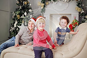 Three happy children in santa caps lie on couch