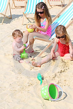 Three happy children sit on beach and play with