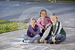 Three happy children sitting on driveway