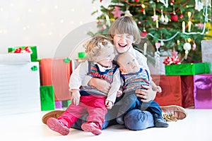 Three happy children - teenager boy, toddler girl and their newborn baby brother - playing together under Christmas tree