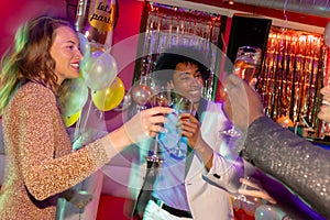 Three happy, diverse male and female friends making a toast with glasses of champagne at nightclub
