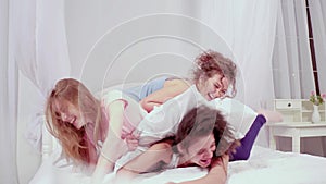 Three happy female best friends lying on bed and looking at camera. Pillow fight charming girls spending leisure time at