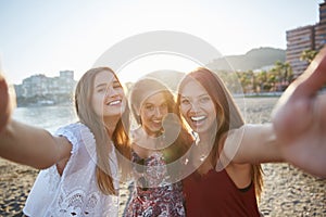 Three happy female friends taking selfie on beach