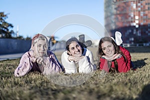 Three happy female girls lying on the grass in a public park at the city