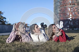 Three happy female girls lying on the grass in a public park at the city