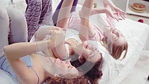 Three happy female lying on bed and looking at the ceiling. Three young girls smiling telling a jokes. Free time concept