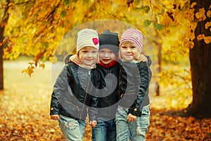 Three happy friends kids hugging and laughing in autumn park