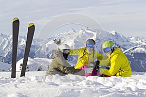 Three happy friends snowboarders and skier are having lunchtime on ski slope in sunny day in the mountains