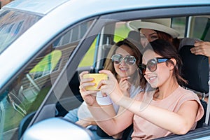 Three happy girlfriends go on a trip. Women are driving in a car and taking a selfie on a mobile phone