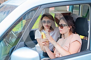 Three happy girlfriends go on a trip. Women are driving in a car and taking a selfie on a mobile phone