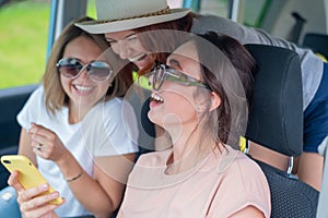 Three happy girlfriends go on a trip. Women Ride in the car, look at the phone and laugh.