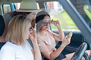 Three happy girlfriends go on a trip. Women Ride in the car, look at the phone and laugh.