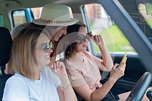 Three happy girlfriends go on a trip. Women Ride in the car, look at the phone and laugh.