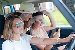 Three happy girlfriends go on a trip. Women Ride in the car, look at the phone and laugh.