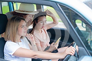 Three happy girlfriends go on a trip. Women Ride in the car, look at the phone and laugh.