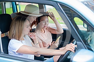 Three happy girlfriends go on a trip. Women Ride in the car, look at the phone and laugh.