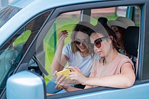 Three happy girlfriends go on a trip. Women Ride in the car, look at the phone and laugh.