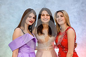 Three happy girls in elegant dresses posing on abstract background. Celebration concept