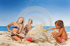 Three happy girls friends sculpting sandcastle